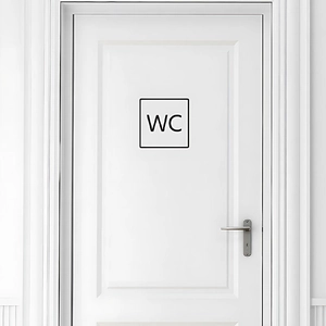 Minimalist square black and white WC sign mounted on a modern white wooden door