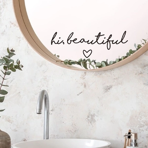 Close-up of 'hi, beautiful' mirror decal on wooden frame in a bright bathroom setting