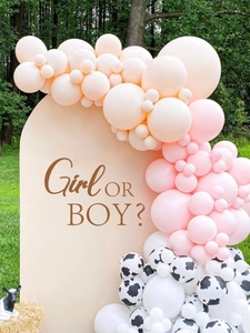 Detail of gender reveal balloon arch with pink and cow print decor on cream backdrop