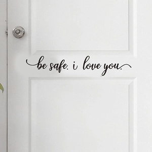 Gros plan du sticker mural 'be safe. i love you.' noir sur une porte blanche