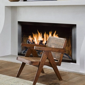 Classic wooden armchair with woven rattan backrest placed by a warm fireplace