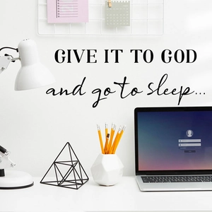 Black 'GIVE IT TO GOD' wall decal quote above a minimalist workspace with a desk and lamp