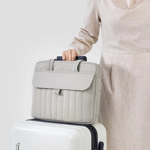 Borsa porta PC grigia trapuntata su una valigia bianca per viaggi e pendolarismo