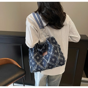 Detailed close-up of blue denim star tote bag with metal chain strap and frayed edges