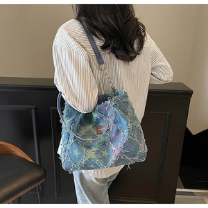 Detailed close-up of blue distressed denim tote bag with star patterns and metal chain