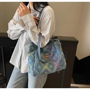 Detail of blue denim tote bag with colorful stars, frayed edges and leather strap