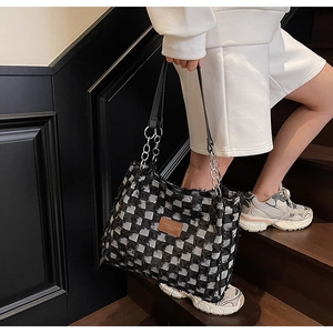 Close-up of checkered denim tote bag with leather logo patch and metal chain strap