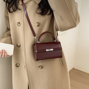 Detail of burgundy PU leather crossbody bag with silver metal buckle and rotating lock