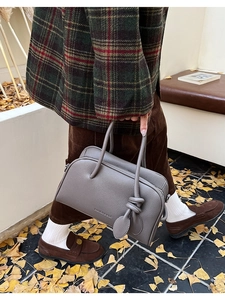 Makroaufnahme einer grauen Boston-Tasche aus Leder mit Blattanhänger und Logo