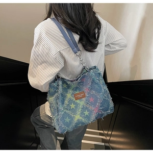 Detail view of denim tote bag with frayed star patterns and leather strap decoration