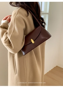 Chic retro dark brown shoulder bag with golden oval buckle worn with a beige coat