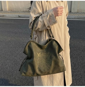 Detail of olive green tote bag featuring gold embroidered daisy and Maodi typography