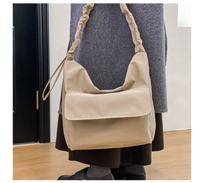 Detail of beige hobo bag showing wide pleated shoulder strap and large front flap pocket