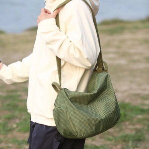 Détail d'un sac bandoulière en toile à carreaux verts avec sangle large et poche zippée