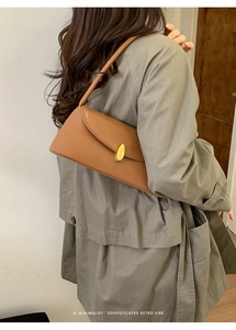 Sophisticated retro caramel brown shoulder bag with a gold metal clasp on an olive coat