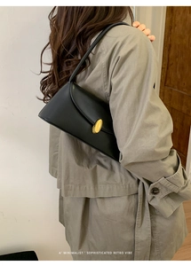 Minimalist black leather underarm bag with gold oval buckle shown in a lifestyle setting