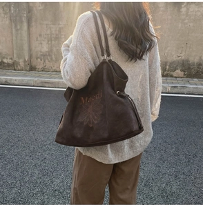 Detailed close-up of dark brown suede tote bag with floral embroidery and drawstrings