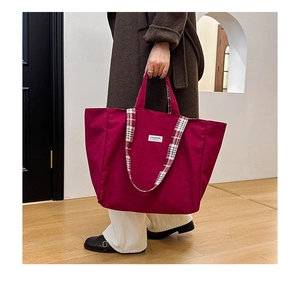 Détail du cabas en toile rouge avec écusson fashion et bandoulière à carreaux