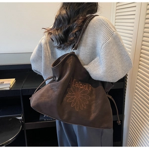 Detail of large dark brown tote bag with floral embroidery and drawstring design on model