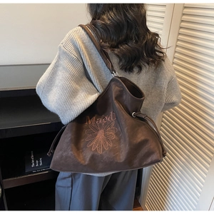 Close-up of dark brown suede tote bag featuring daisy embroidery and drawstring detail