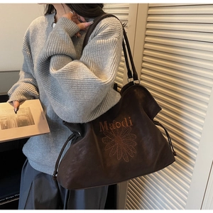 Detail of embroidered daisy and Maodi logo on dark brown suede shoulder tote bag