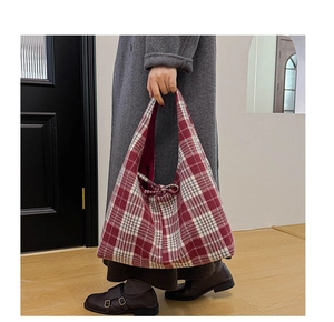 Detail of a red and white plaid tote bag with tie-up closure on a model in gray coat