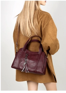 Detail view of burgundy crossbody bag with woven handle, tassel and cat pendant accessory