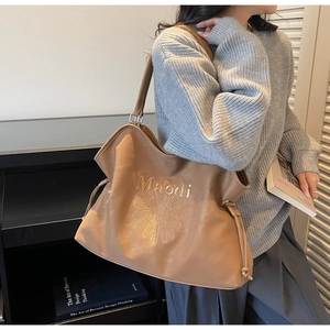 Detail of camel leather tote bag featuring daisy embroidery and side drawstring design