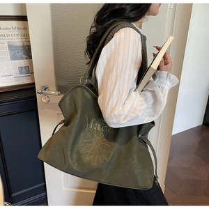 Detail shot of green suede tote bag with flower embroidery and drawstring on model