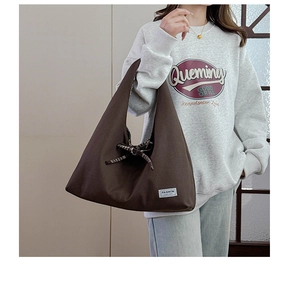 Detail of a large brown canvas tote bag featuring a plaid bow and fashion brand label