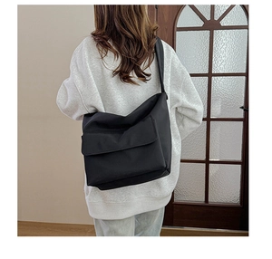 Rear view of a model wearing a large black nylon messenger bag for casual daily commuting
