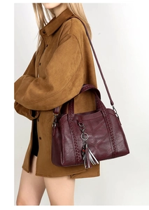 Detail view of burgundy leather handbag with woven handle and fringe pendant on model
