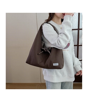 Detail of a brown canvas tote bag featuring a white logo patch and a side bow knot detail