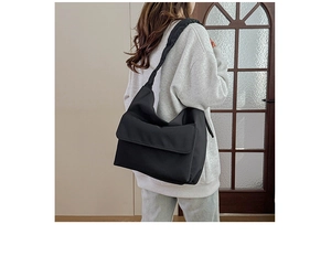 Detail of minimalist black nylon messenger bag with wide shoulder strap and large flap closure