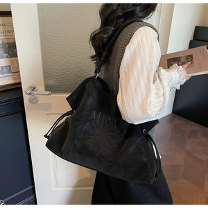 Detail of black tote bag featuring daisy embroidery and drawstring closure on shoulder strap