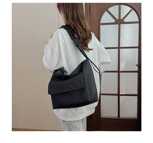 Detail of black nylon crossbody bag featuring a wide ruched strap and large front flap pocket