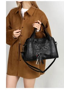 Detail of black leather handbag with woven handle, fringe charm and V-shaped stitching