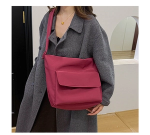 Deep pink nylon messenger bag with front pocket shown on dark grey wool coat