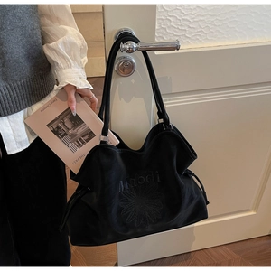 Close-up of black suede tote bag with embroidered floral daisy and drawstring closure