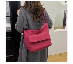 Detail view of large rose red nylon crossbody bag with flap pocket on shoulder