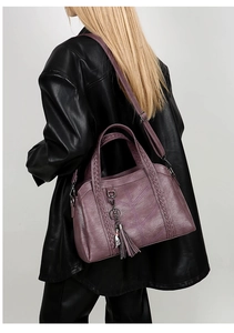 Detail of purple crossbody bag with braided handles and metal cat charm shown on model