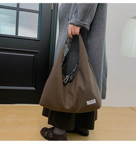 Detail of a large brown canvas tote bag featuring an inner blue plaid lining and brand label