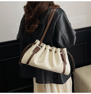 Detail of pleated beige tote bag featuring a brown shoulder strap and cute bear charm