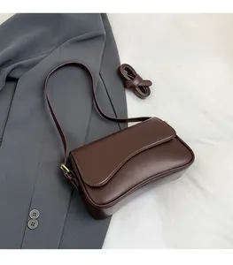 Detail of dark brown matte leather baguette bag with curved flap and adjustable shoulder strap