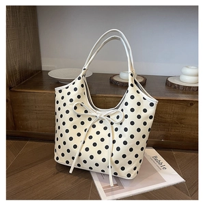 Stylish white polka dot tote bag with black bow detail for women in a cozy home setting