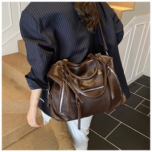 Detail of dark brown faux leather tote with silver zippers and stylish long fringe tassels