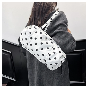 Sac à bandoulière minimaliste à pois noirs porté par un mannequin en milieu urbain