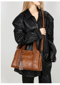 Close-up of brown vintage leather bag with woven details and metal tassel on a model