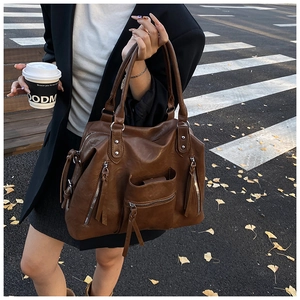 Close-up of vintage brown PU leather handbag with metallic zippers and long tassels