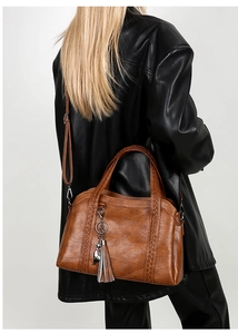 Close-up of caramel leather bag featuring woven details and metal cat charm